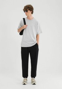 Szara koszulka z krótkim rękawem w zestawieniu z czarnymi zwężającymi się spodniami, prezentująca prosty design. Dodatki to czarne okulary przeciwsłoneczne oraz jasne sneakersy.