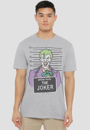 Man wearing gray t-shirt with a colorful Joker mugshot graphic and “Gotham Police The Joker” sign on front.