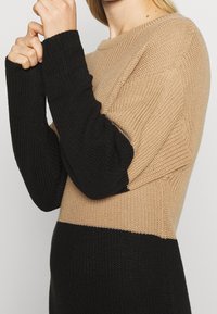 Stickad tröja med färgblockdesign där beige är på toppen och svarta ärmar och nederdel, texturerad tyg och långa ärmar.