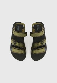 Grønne sandaler med tre justerbare remmer, sort såle og teksturert fot seng. Har søm detaljer og merkevarelogo på fot sengen.