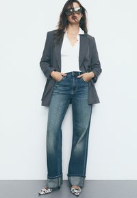 Šedý blazer přes bílý v-neck top, doplněný vysokými, širokými vybledlými džíny. Zdobeno vzorovanými vysokými podpatky.