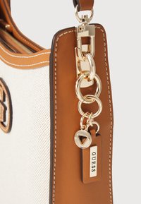 Sac à main beige et blanc avec des détails en chaîne dorée. Présente un accent logo, une texture lisse et des coutures contrastées sur les bords.