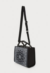 Sort stofpose med et paisley-design på den ene side, prydet med korte håndtag og en aftagelig justerbar rem. Fyrkantet form, glat tekstur.