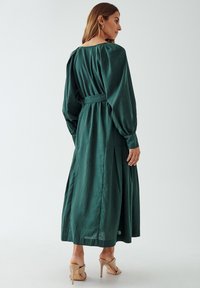 Green, long-sleeve dress with a cinched waist, pleated skirt, and soft texture. Features puffed sleeves and a round neckline.