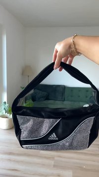 Svart nylonveske med bredt håndtak, med en front pyntet med rhinestones og en kontrastfarget hvit glidelås. Adidas-logoen vises fremtredende.