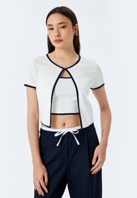 Wit geribd crop top met korte mouwen en marineblauw randje, met een open voorkant en een ronde halslijn, gecombineerd met marineblauwe joggingsbroek met trekkoord.