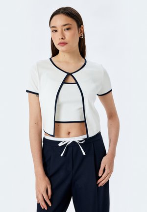 Biała prążkowana crop top z krótkim rękawem i granatowymi wykończeniami, z otwartym przodem i okrągłym dekoltem, w zestawie z granatowymi spodniami z troczkiem.