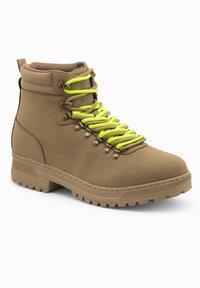 Botas de senderismo impermeables marrones con un collar acolchado, cordones verde brillante, ojales de metal y una suela robusta para mayor tracción.