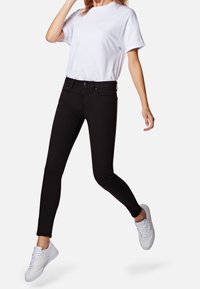 Jeans negros ajustados con una textura suave y bolsillos frontales, combinados con una camiseta blanca de cuello redondo y zapatillas blancas.