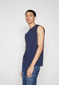 Marineblå ermeløs bomulls t-skjorte med rund hals, som har en avslappet passform og glatt tekstur, kombinert med blå denim jeans.