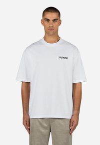 Valge lühikese varrukaga T-särk, mis on valmistatud puuvillast, ümarate krae ja musta „PEGADOR“ teksti logoga, mis on trükitud vasakule rinda.