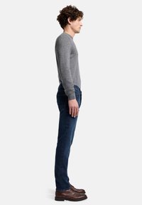 Graues Langarmshirt kombiniert mit dunkelblauen Jeans und braunen Schuhen. Sichtbare Nahtdetails und eine taillierte Silhouette. Seitenansicht.