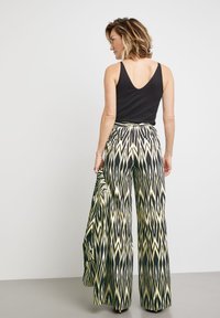 Black tank top paired with wide-leg trousers featuring a zigzag pattern in green, yellow, and black. The pants have a high waist and pockets.