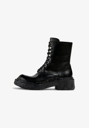 Botte de combat en cuir noir à lacets, avec un bout arrondi et une semelle épaisse et texturée. Dotée d'œillets en métal et d'un tige de hauteur intermédiaire.