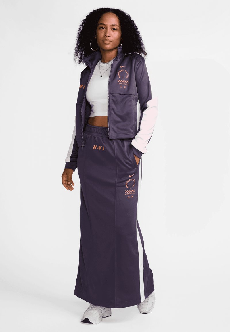 Chándal deportivo de color púrpura oscuro con detalles en blanco, que incluye una chaqueta con cremallera y una falda larga, adornado con logotipos de Nike en un color de contraste.