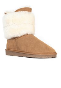 Brun mockasinhöga stövel med en fluffig krämfärgad pälskant, rund tå och platt gummisula. Ovandelen har en slät yta.