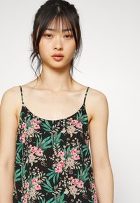 Camisola floral preta com alças finas. Apresenta flores e folhas em rosa e verde num tecido texturizado. Design casual, ajuste solto.