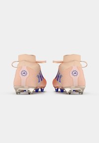 Botas de fútbol color melocotón claro con diseño estriado, acentos azules, cuello alto y tachuelas plateadas en una suela texturada. Incluye detalle del logo en la parte trasera.