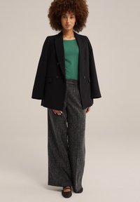 Svart dubbelknäppt blazer med breda slag, grön figurnära topp, grå strukturerade vida byxor och svarta platta skor.