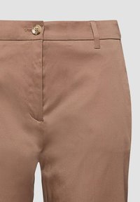 Pantalon beige avec fermeture à bouton et passants pour ceinture, présentant un tissu lisse et des coutures nettes sur la ceinture et le devant.