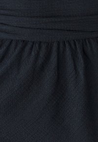 Schwarzer Stoff mit einer strukturierten, zerknitterten Optik. Verfügt über eine geraffte Taille, die eine fließende Silhouette erzeugt. Leichtes Material.