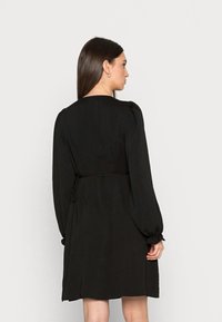 Vestido preto com decote redondo, mangas bufantes longas e cintura amarrada. Feito de um tecido texturizado, apresenta um desenho até ao joelho.