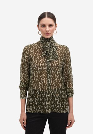 Blusa verde transparente con patrón de lunares y alto cuello con volantes, que presenta mangas largas y cierre frontal con botones.