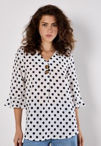 Weißes Bluse mit marineblauen Punkten, V-Ausschnitt, dreiviertel länge ausgestellte Ärmel und drei dekorative Knopfakzente auf der Vorderseite.