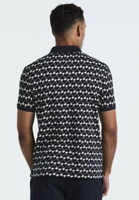 Polo à manches courtes en navy avec un motif géométrique de diamants blancs. Doté d'un col en maille et d'un tissu texturé. Vue de dos présentée.