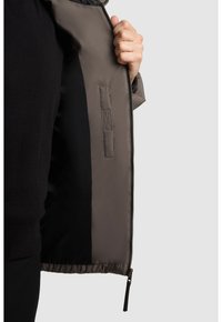 Giacca da uomo in tessuto grigio, con una superficie liscia, chiusura con zip e una tasca interna con dettaglio di cucitura, che rivela una fodera nera.