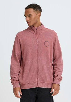 Rød hættetrøje med lynlås fremstillet af tekstureret stof, med høj krave, ribstrikkede ærmeafslutninger og en rund logo på brystet. Klassisk pasform.