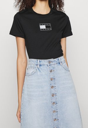 Czarna koszulka z krótkim rękawem z logo "TOMMY JEANS" w prostokątnym wzorze, w połączeniu z jasnoniebieską spódnicą dżinsową z guzikami z przodu.