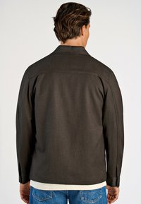 Donkerbruine jas van een gestructureerde stof, met een klassieke kraag, lange mouwen en knoopmanchetten, gecombineerd met lichtblauwe jeans.