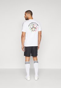Balta īsām piedurknēm T-kreklu ar "JUVENTUS" logo aizmugurē, apvienots ar melnām šortiem, kuros ir krāsainas sānu svītras, un svītrainām baltām zeķēm.