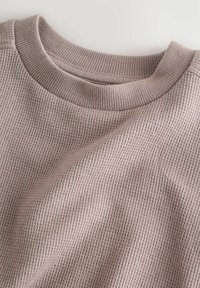 Svetloružový rebrovaný sveter s okrúhlym výstrihom, mäkkou textúrou a viditeľnými vertikálnymi pruhmi v látke.
