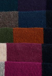 Textil con secciones rectangulares en varios colores: azul oscuro, verde, naranja, púrpura, burdeos, crema y negro, con una textura de lana.