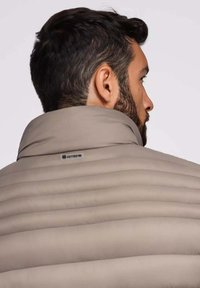 Beige pufferjack met hoge kraag, horizontaal gestikt patroon en een logolabel op de achterkant van de halslijn. Glad stofafwerking.