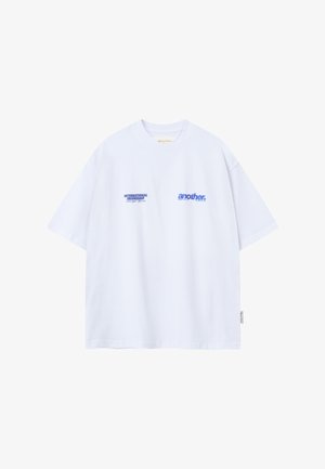 Camiseta blanca oversize con texto azul "AMISTAD INTERNACIONAL a través del deporte" y "another" en el frente, mangas cortas, cuello redondo.