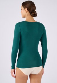 Camicia a maniche lunghe di colore verde scuro, design aderente, realizzata in un tessuto morbido, con scollatura tonda e schiena liscia, senza cuciture.