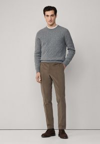 Maglione grigio a trecce, pantaloni slim-fit marroni e scarpe stringate marroni. Design semplice, maglia testurizzata e colori neutri.