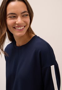 Sweatshirt bleu marine avec un col rond, en tissu texturé, et des rayures blanches contrastantes sur les manches. Design simple et moderne.