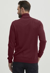 Bordeaux pullover-neule, jossa on korkea kaulus, pitkät hihat sekä resorit hihansuissa ja helmassa. Silkkinen rakenne, jossa on minimoitu ommelkoristelu.