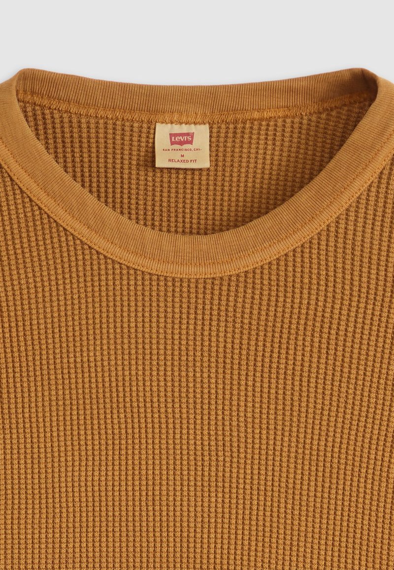 Entspannt geschnittenes, senfgelbes Langarmshirt aus strukturierter, gerippter Stoff mit Rundhalsausschnitt und sichtbarem Etikett, das innen angenäht ist.