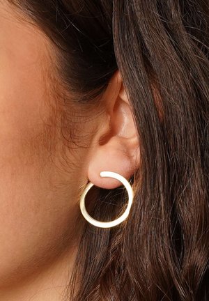 Goldene Creole, die am Ohr eines Models präsentiert wird, mit einem glatten, abgerundeten Design und einem offenen Segment für einen modernen Look.