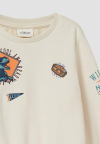 Cremefarbener Pullover mit geripptem Halsausschnitt; zeigt Dinosaurier- und Abzeichen-Grafiken sowie bunte Texte und dreieckige Designs.