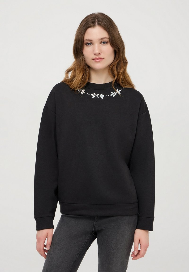 Czarna bluza z miękkiego materiału, z okrągłym dekoltem i haftem kwiatowym na kołnierzu. Luźny krój z długimi rękawami i mankietami.