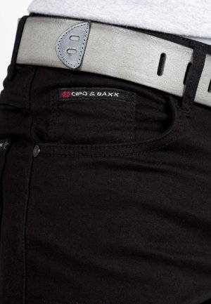 Black jeans with a close-up of a grey leather belt featuring a smooth texture and rounded hardware. Brand logo visible on the jeans.