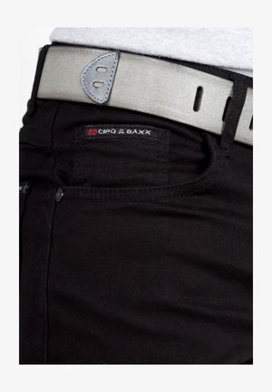 Black jeans with a close-up of a grey leather belt featuring a smooth texture and rounded hardware. Brand logo visible on the jeans.