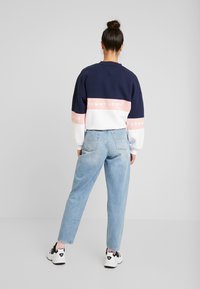 Sudadera recortada en azul marino y blanco con una franja rosa que presenta el texto "TOMMY JEANS", combinada con jeans de tiro alto en azul claro y zapatillas negras.