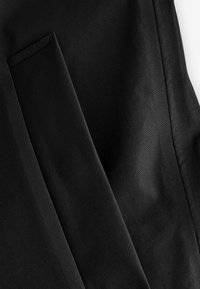 Tissu noir avec une texture lisse et mate. Présente une poche et des coutures nettes et droites. Met l'accent sur la couleur uniforme et l'absence de motifs.